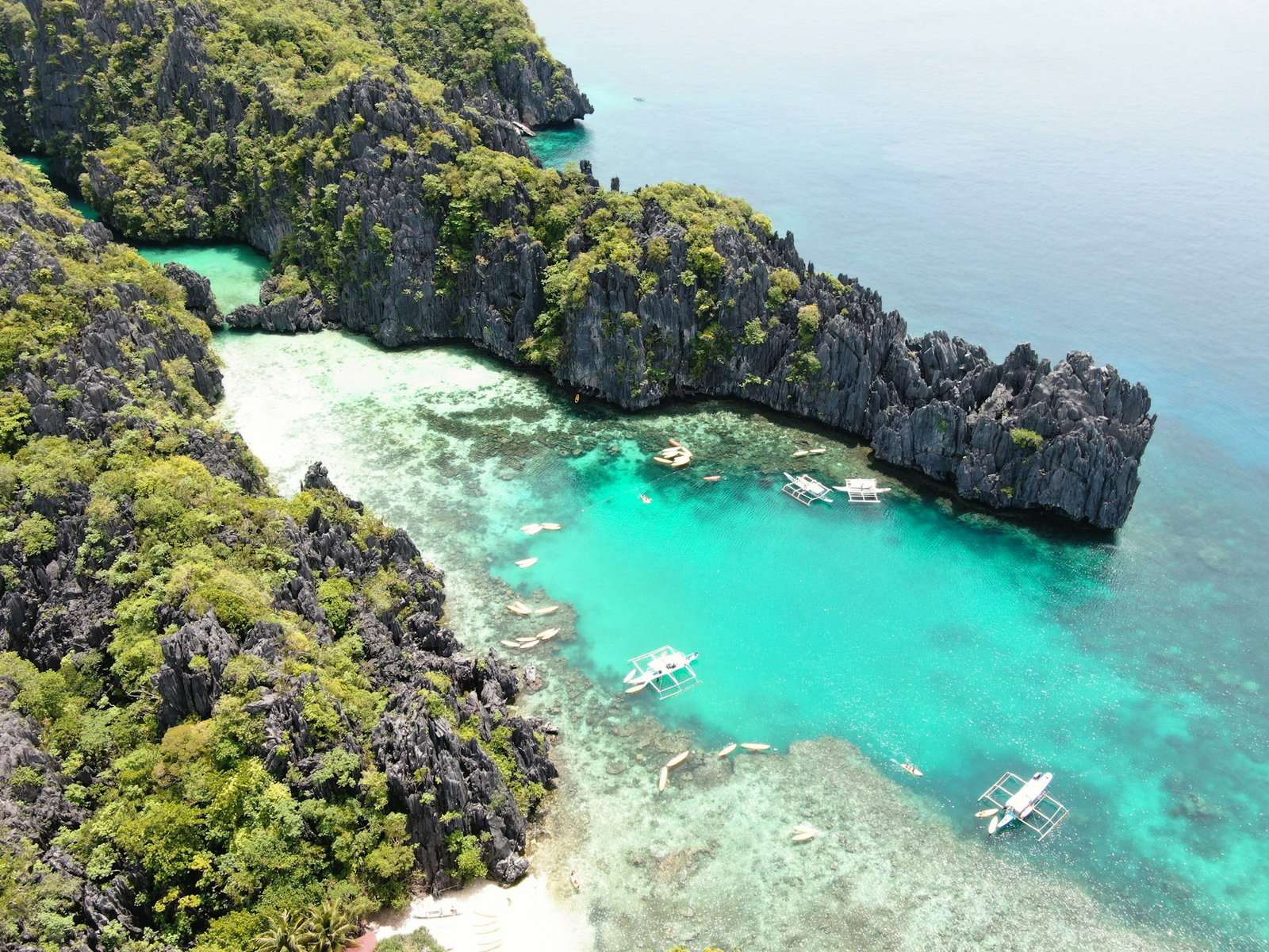 Aerial shot of rocky grey cliffs covered in green jungle with bright turquoise waters and traditional boats