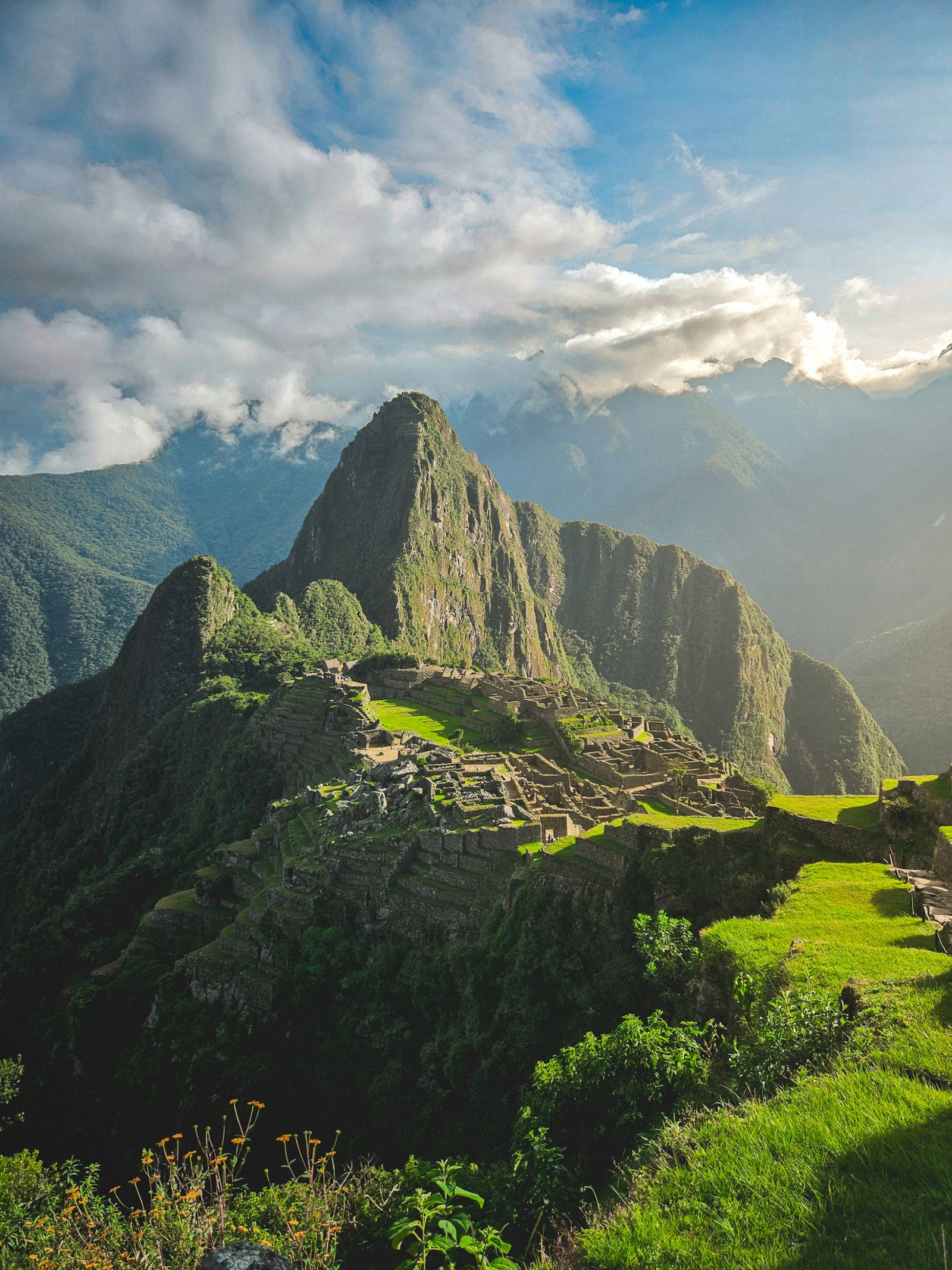 Emerald grass with terraced hilltops leading into epic ruin site and surrounded by mountains on cloudy morning at sunrise