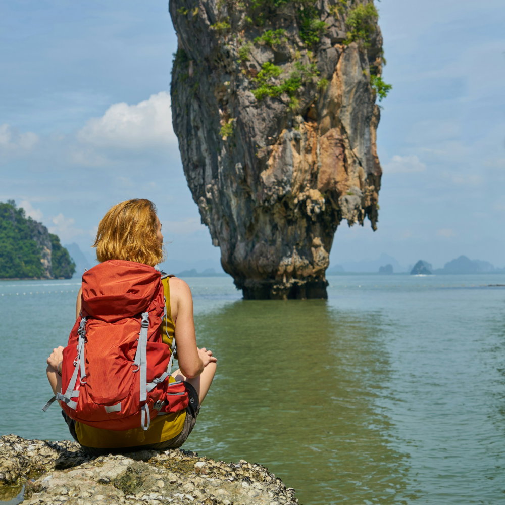 Traveller sitting on a rock overlooking islands in the water in Thailand