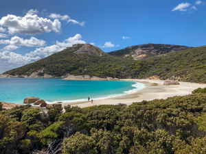 A pristine beach with blue water surrounded bu lush greenery and mountains