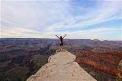 Person stands at a peak with arms outstretched overlooking the Grand Canyon