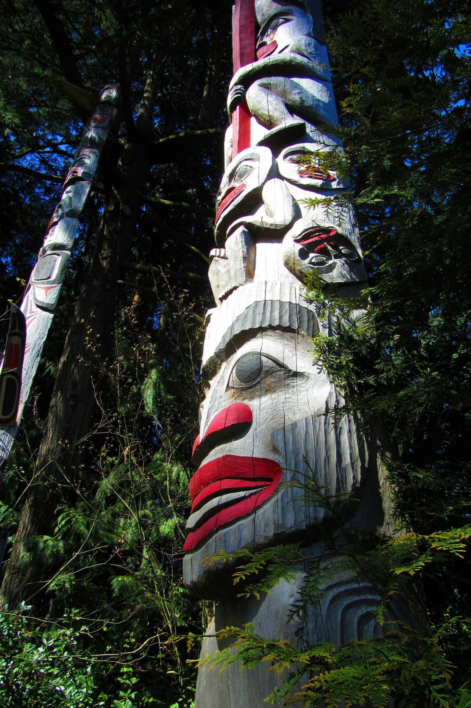 Traditional Totem Pole painted with faces and surrounded by forest trees