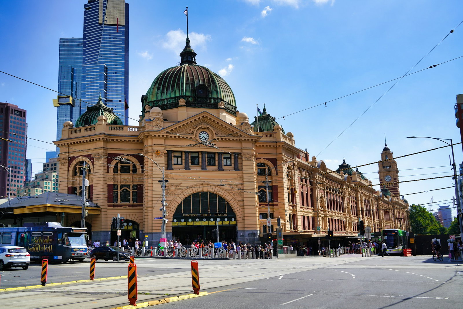 Historic brown train station with round green rooftop and clock tower, with traffic on sunny day, Melbourne
