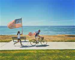A person cycling with an American flag as a cape, followed by a person holding an American flag
