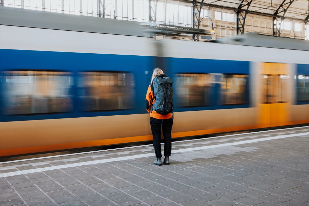 Backpacker at train station as train goes past 