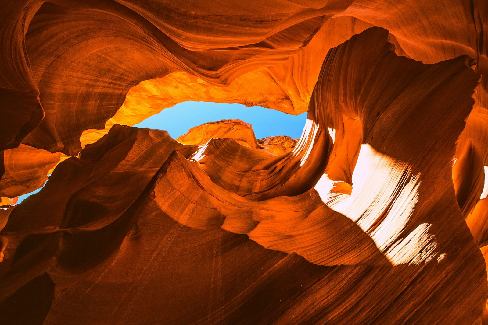 Swirly bright orange cave ceiling with bright blue sky peaking in the centre