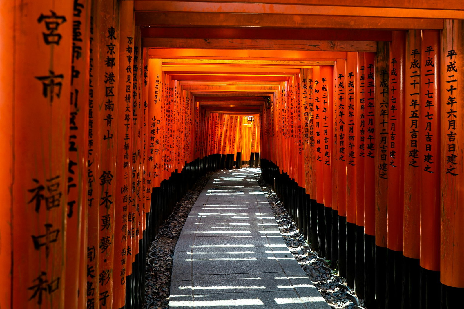 Traditional red shrines with inscriptions lined enxt to each other with a stone path in the centre
