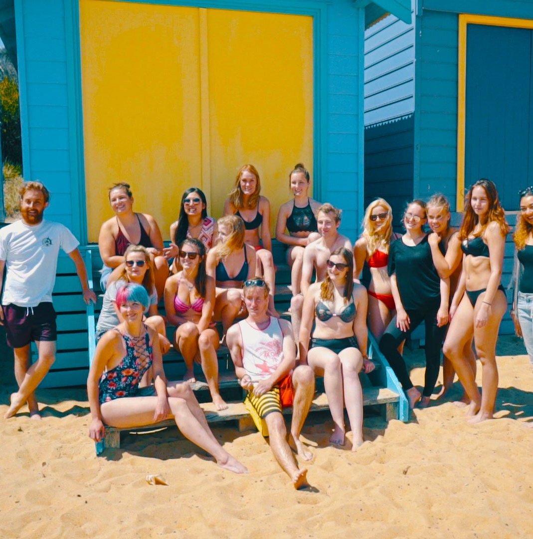 Group of people in swimwear in front of colourful beach huts in Melbourne