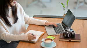Person writing in note book and using laptop