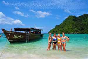 Travellers posing next to traditional thai boat on beach