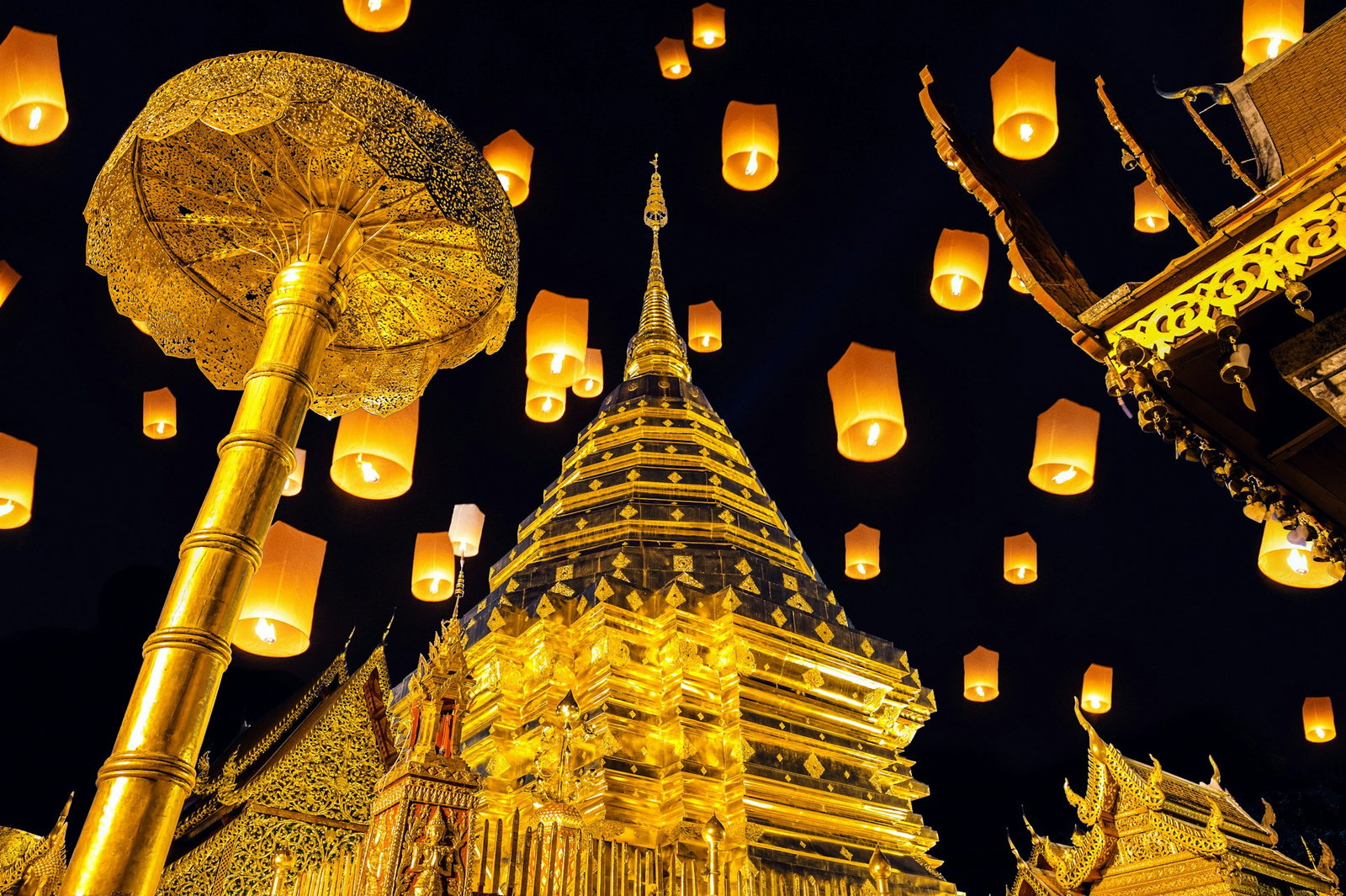 Floating orange lanterns surround golden ornate, traditional temple palace on a pitch black night