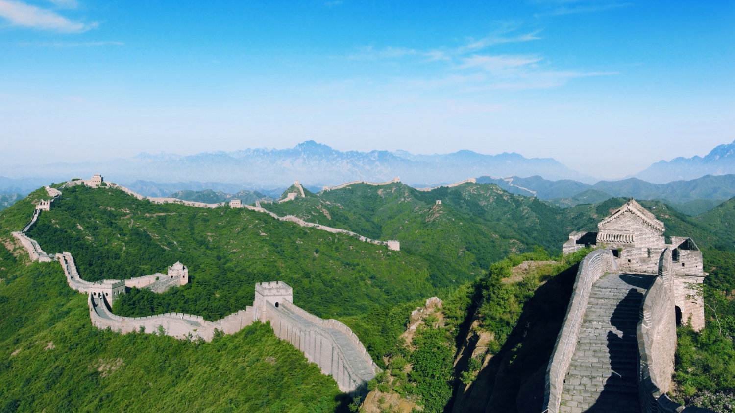 Various historic fortress walls woven through bright green mountains under a blue sky with a gentle mist