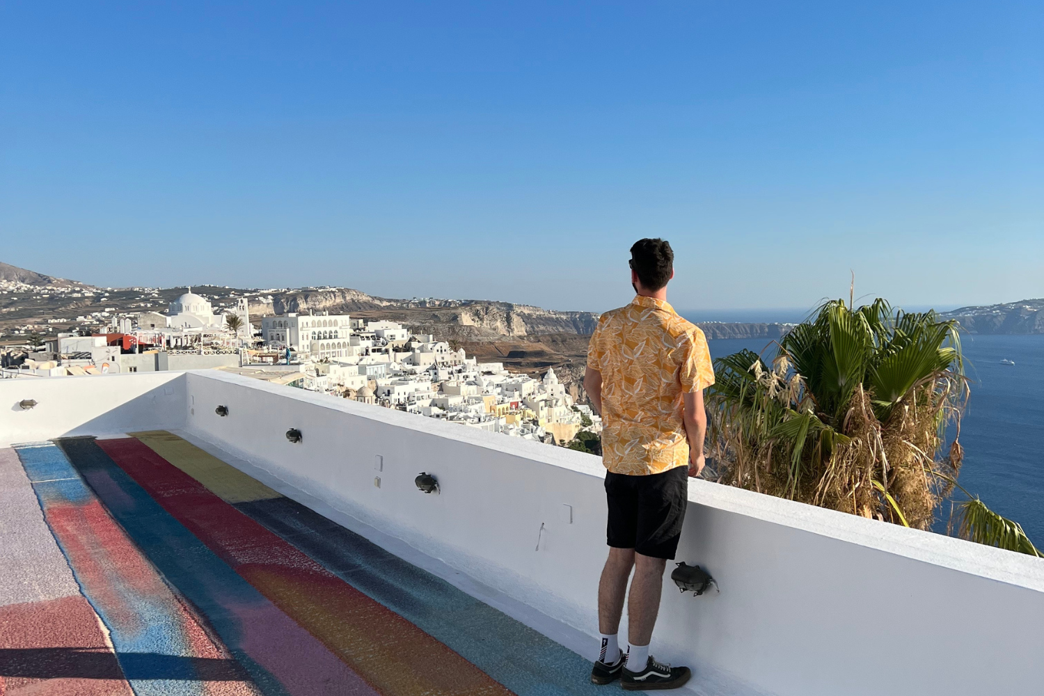 Traveller on a group trip of Greece at a roof top bar in Santorini, looking across the ocean and aesthetic white buildings