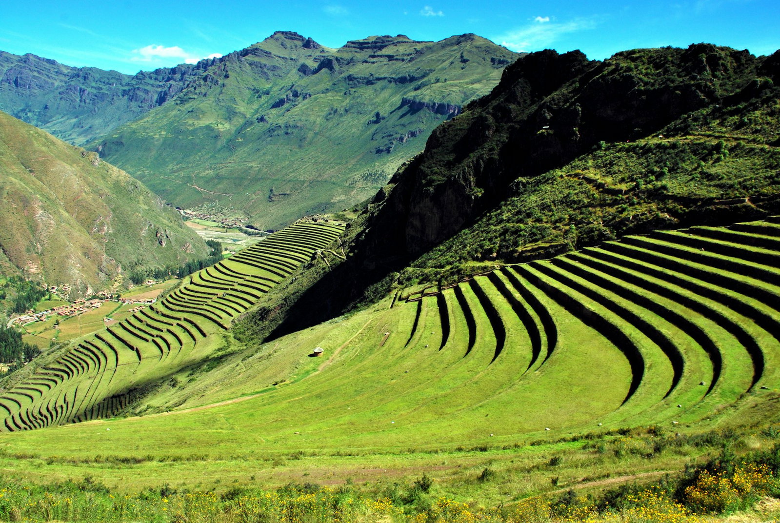 Bright green valley with terraced ruin hills surrounded by green mountaisn and a little village at the bottom with blue skies