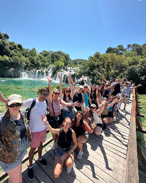 Group of travellers with their arms in the air in front of waterfall in Croatia