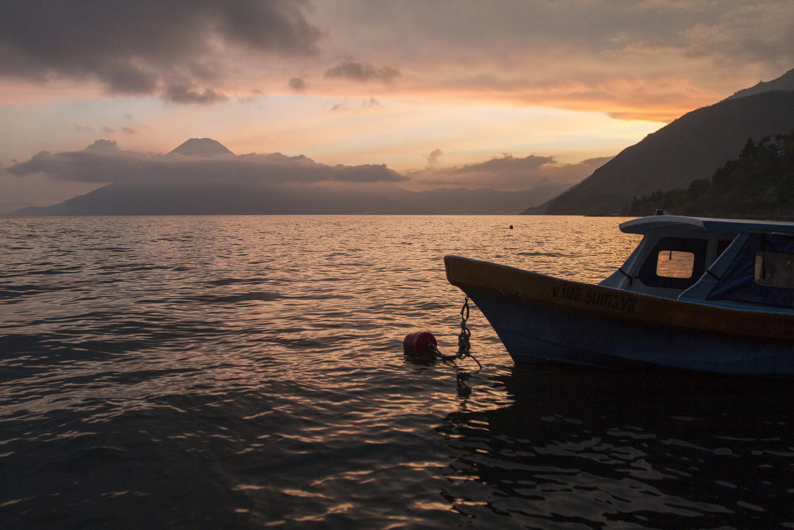 A boat sitting on the water at sunset with a volcano in the distance