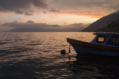 A boat sitting on the water at sunset with a volcano in the distance
