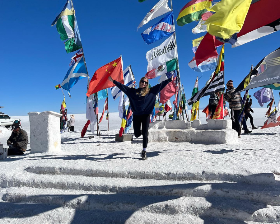 Traveller at the Uyuni Salt Flats with their hands in the air next to the different world flags.