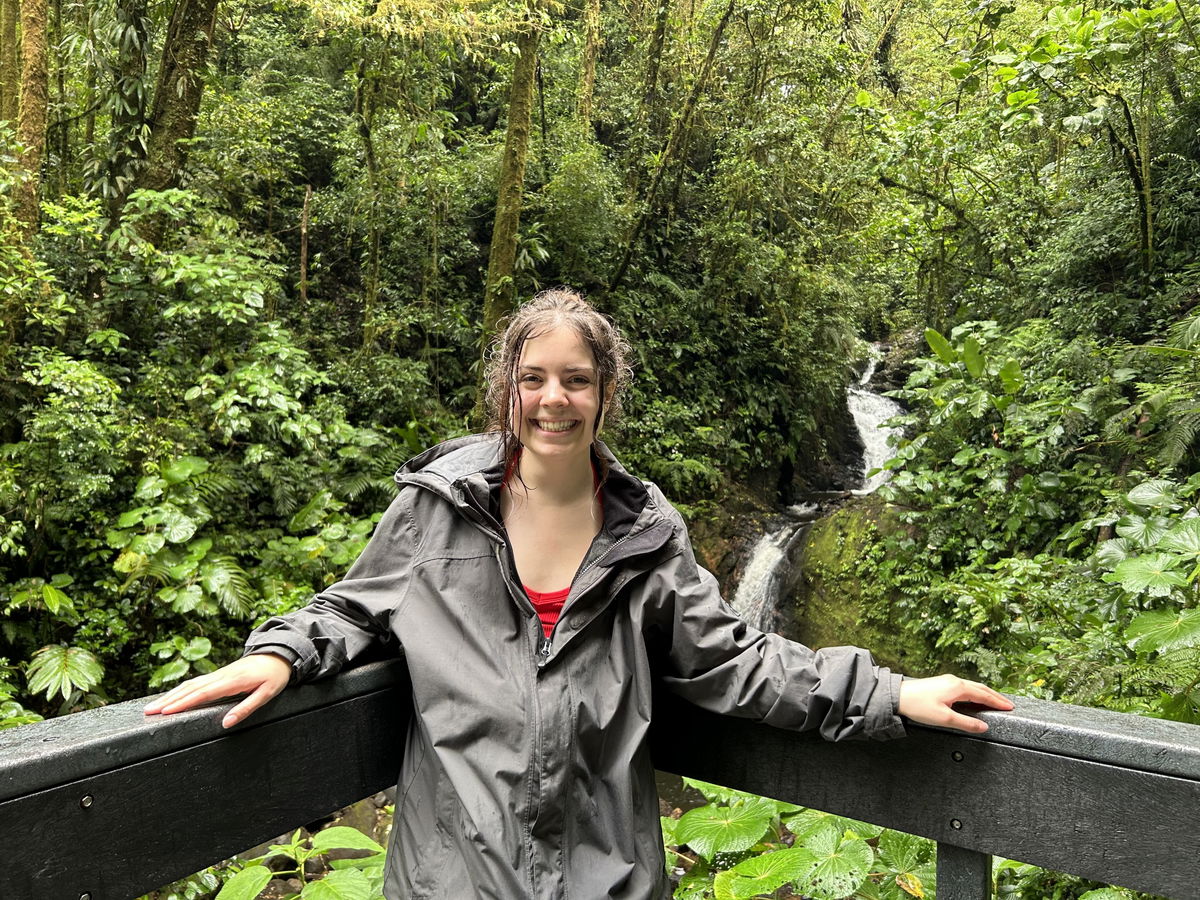 Woman in front of small waterfall in a cloud forest with lots of green trees, Monteverde Cloud Forest, Costa Rica