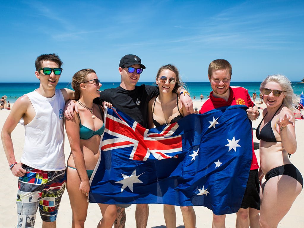 Travellers on a beach holding an Australian flag