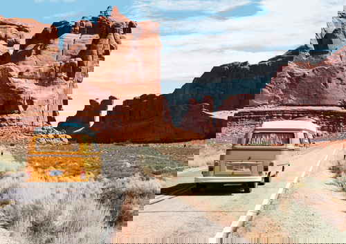 A lone yellow campervan drives in a road between canyons in the USA