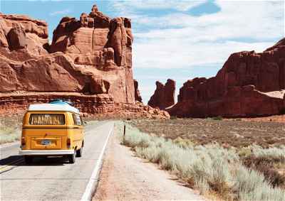 A lone yellow campervan drives in a road between canyons in the USA