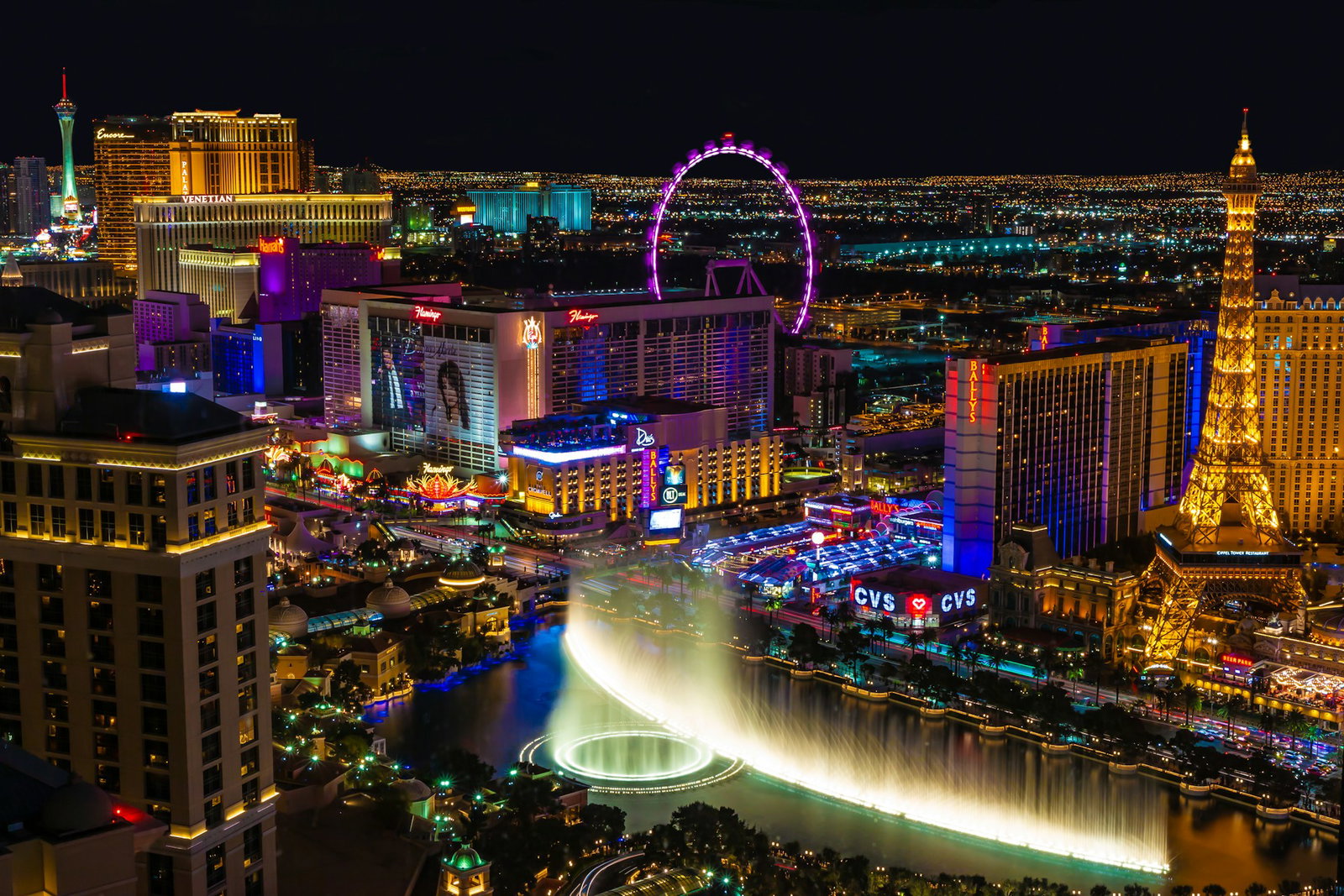 Eclectic cityscape with Eiffel Tower to the right amid neon-lit buildings and fountain, Las Vegas