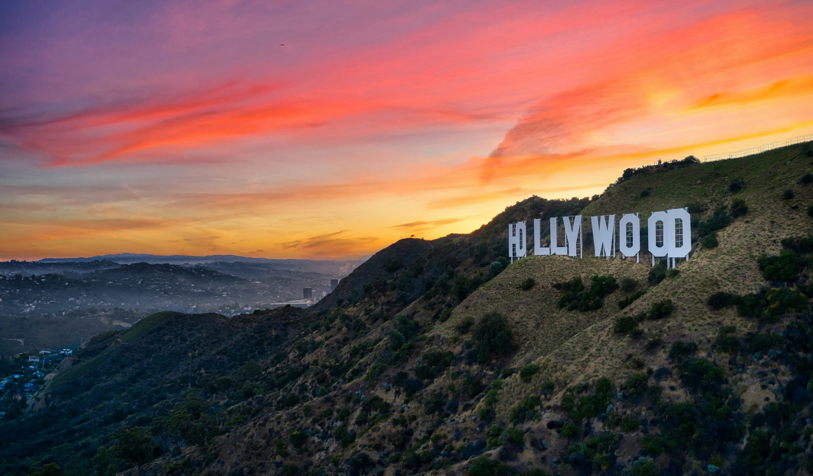 The Hollywood sign on the dry green hill with a beautiful pink and orange sunset over Los Angeles