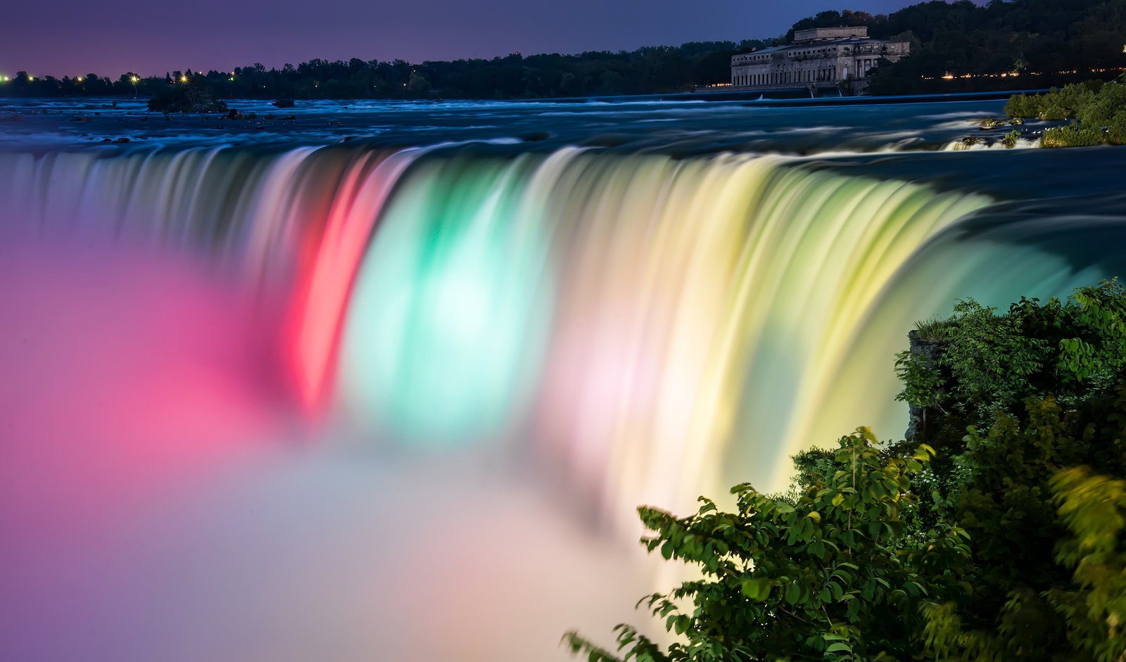 Huge waterfall lit up like a rainbow with tree to the right side, Niagara Falls