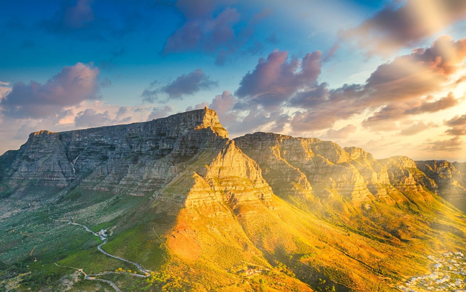 Sunrise over a broad curved mountain top with rocky cliffs and lilac grey clouds in the blue sky, Table Mountain South Africa