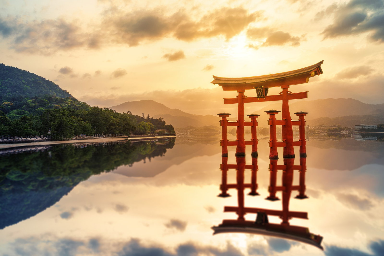 Traditional Japanese shrine in water at sunset with reflections and green hill to the left