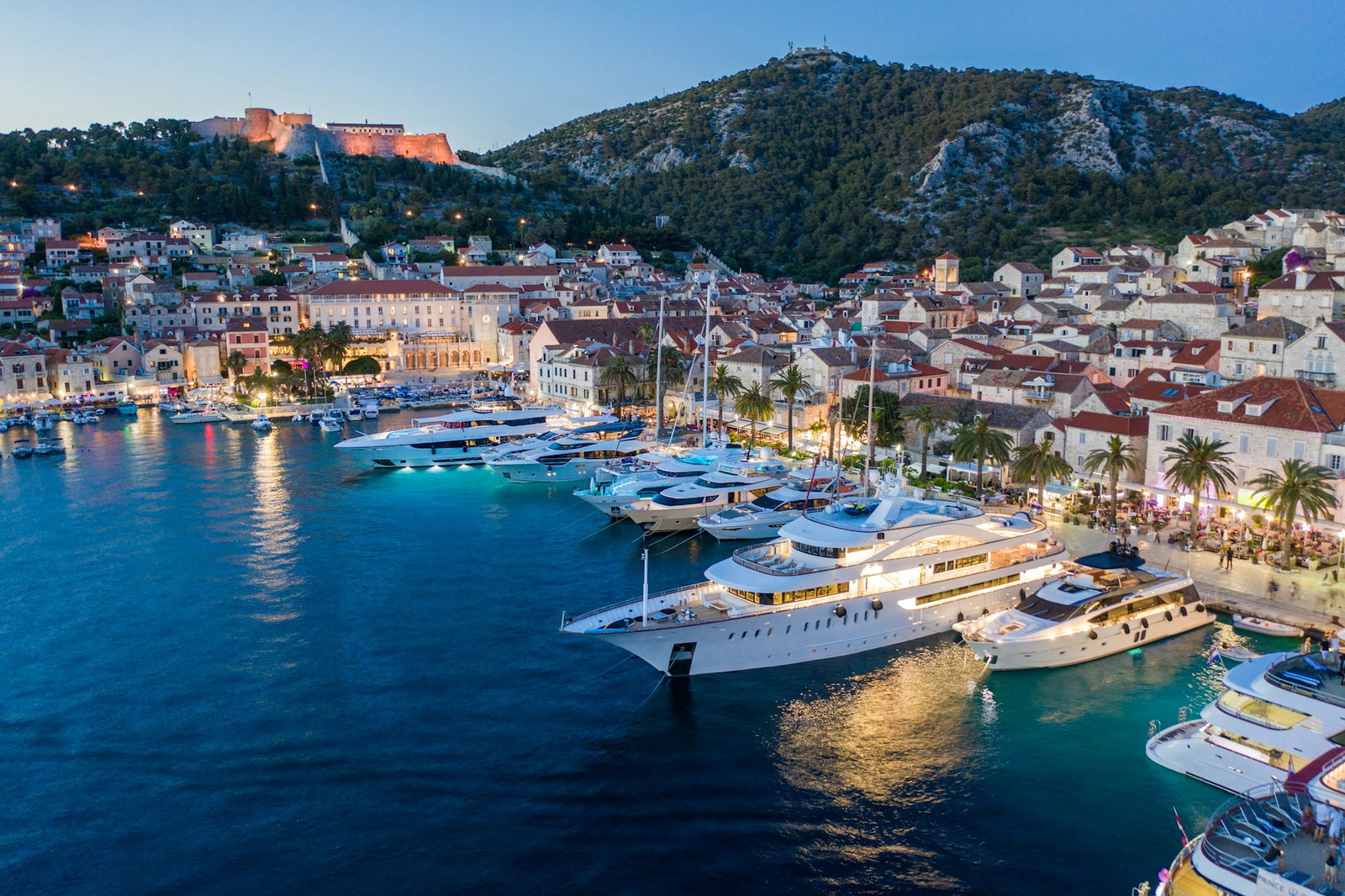 Cruise sailboats docked at harbour in Hvar at nighttime backed by hills and illuminated buildings