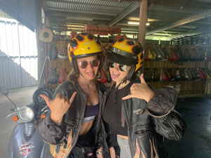 Two travellers with helmets on next to a scooter
