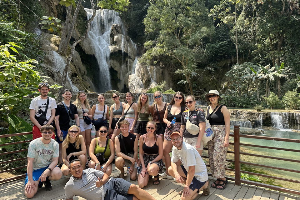Group of travellers and local tour guide smiling in front of waterfall in Laos