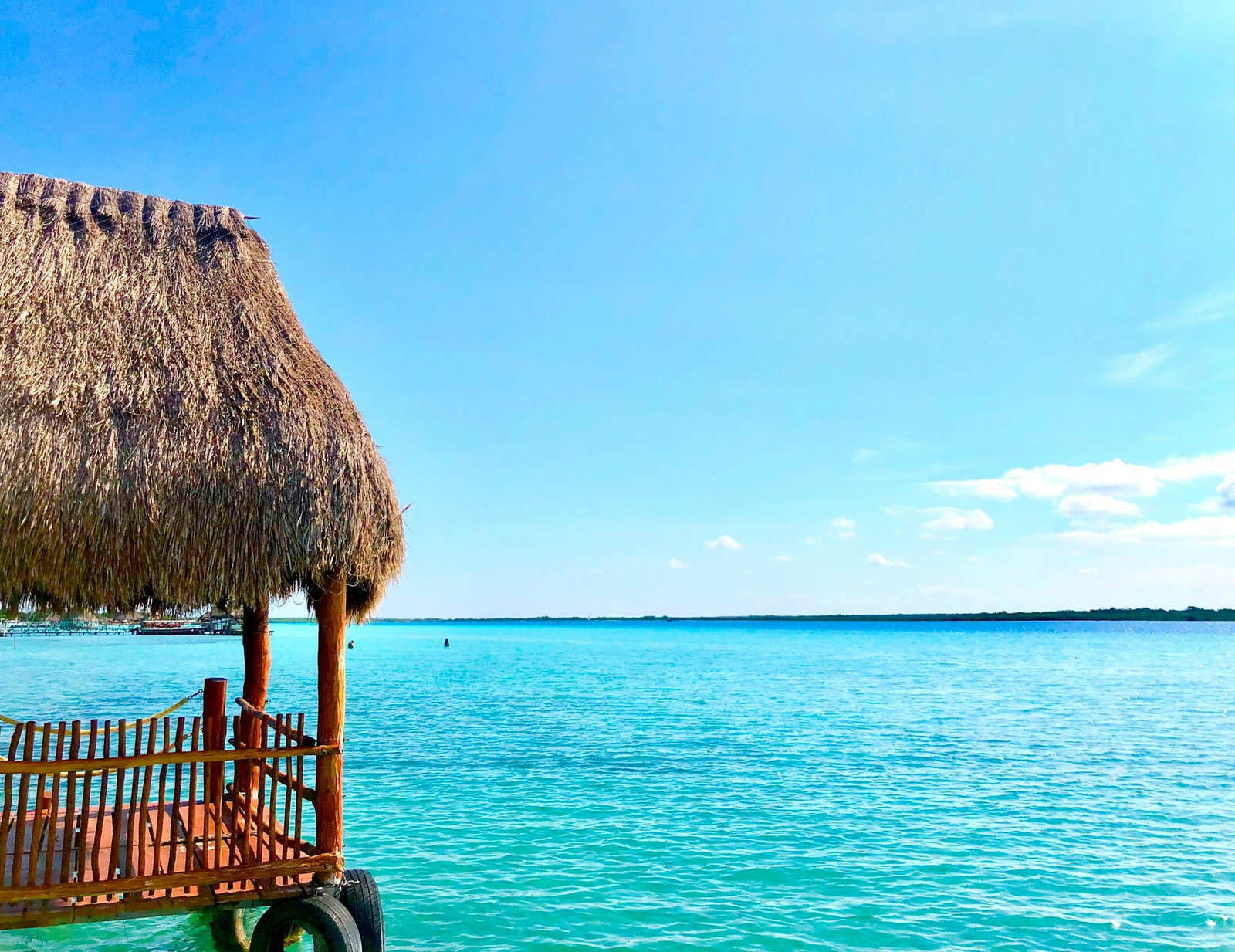 Small wooden shack with rustic roof and tires overlooking bright turquoise ocean on a clear day with some boats to the left