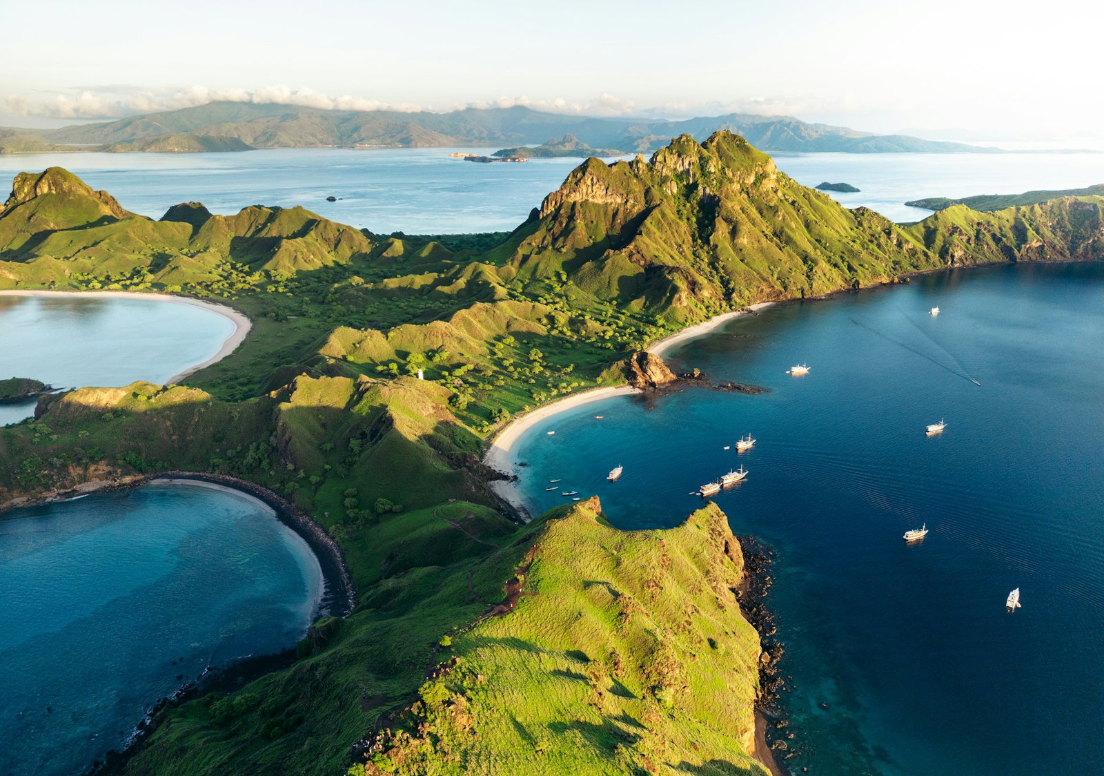 Viewpoint from top of island overlooking emerald volcano cliffs with ocean on both sides and little stretches of rosy sand