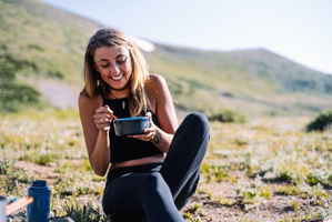 A traveller sitting at the foot of a mountain smiling and eating