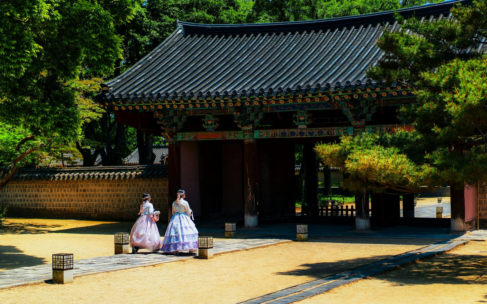Traditional Hanok village with secluded palace grounds and two women dressed in pastel hanbok surrounded by green trees