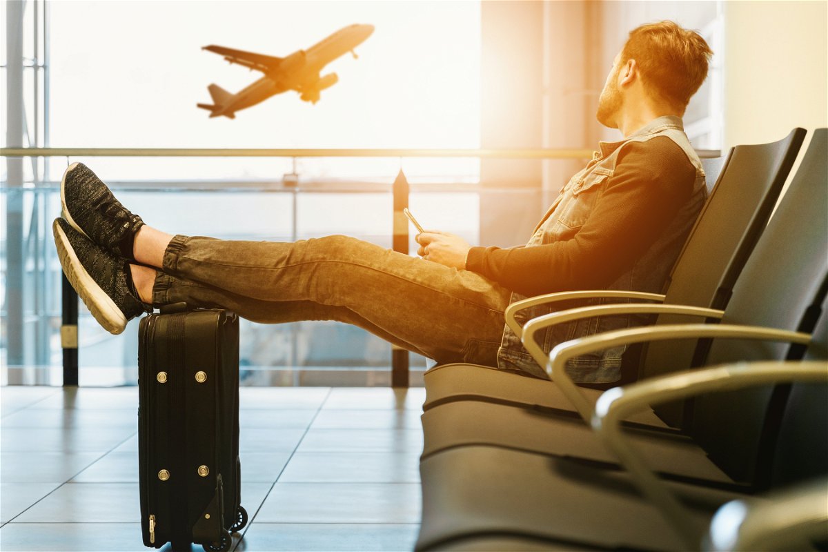 Person waiting for flight with suitcase with plane in background
