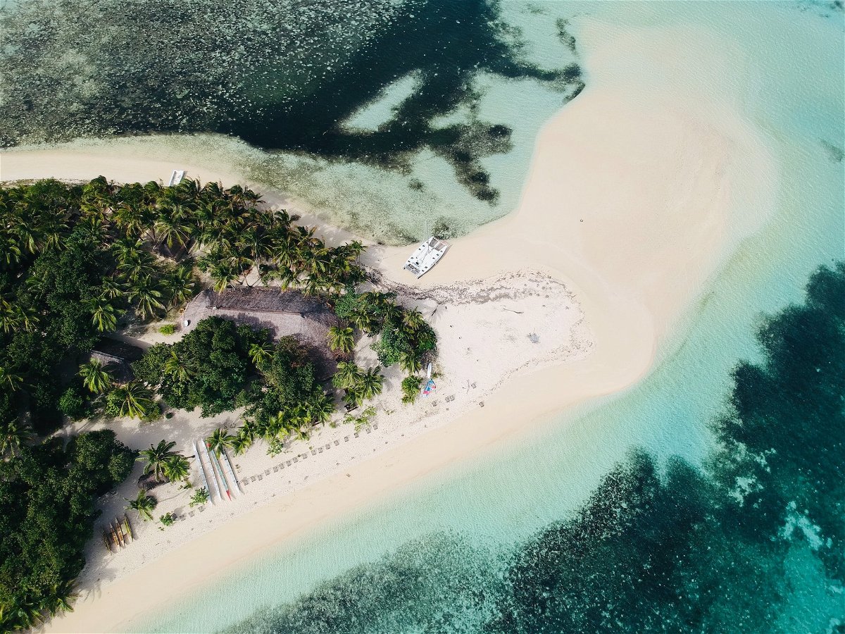 A sandy beach on an island with a lone catamaran