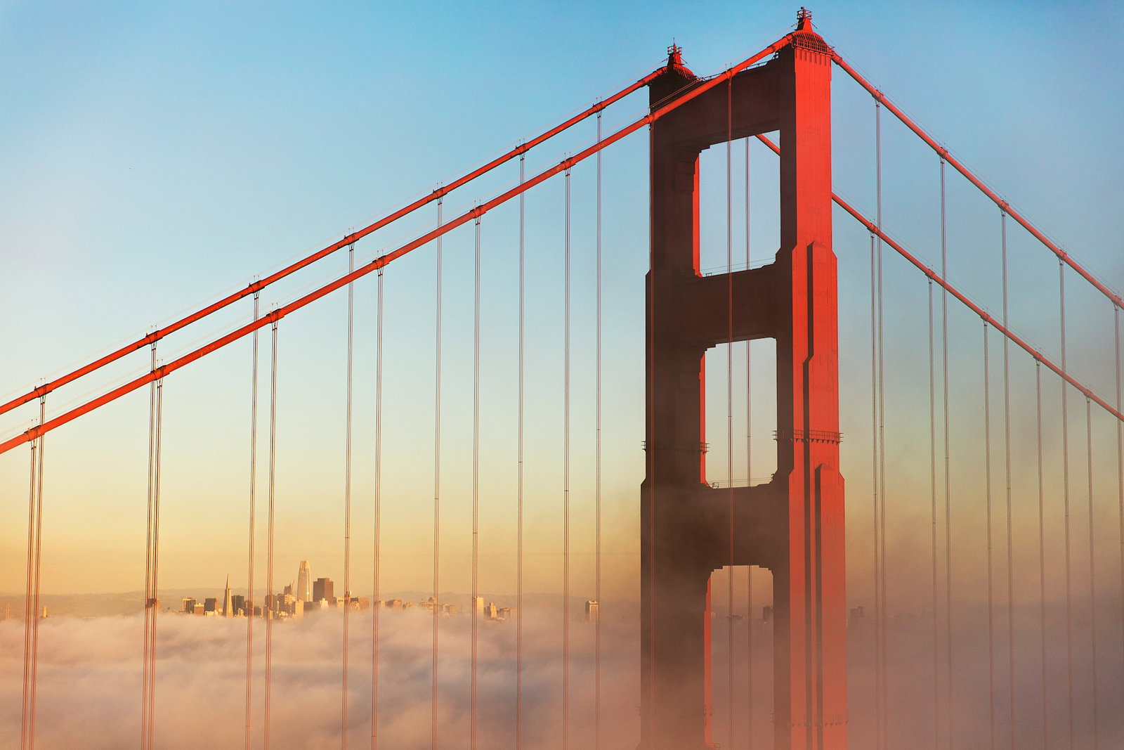 Bright red bridge at misty soft sunrise with city in the distance, San Francisco