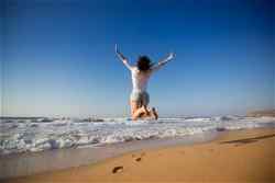 A traveller mid-jump on a beach with crashing waves