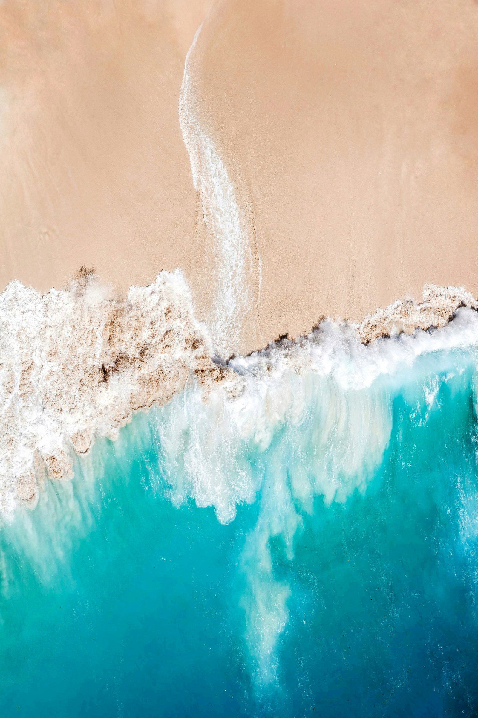 Aerial shot of golden sand beach with crashing waves and bright turquoise ocean, Nusa Penida