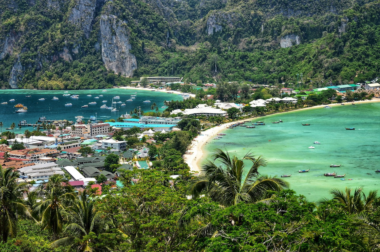 Tropical palm tree valley with low roof city buildings in centre, long beach with lots of boats and high limestone cliffs