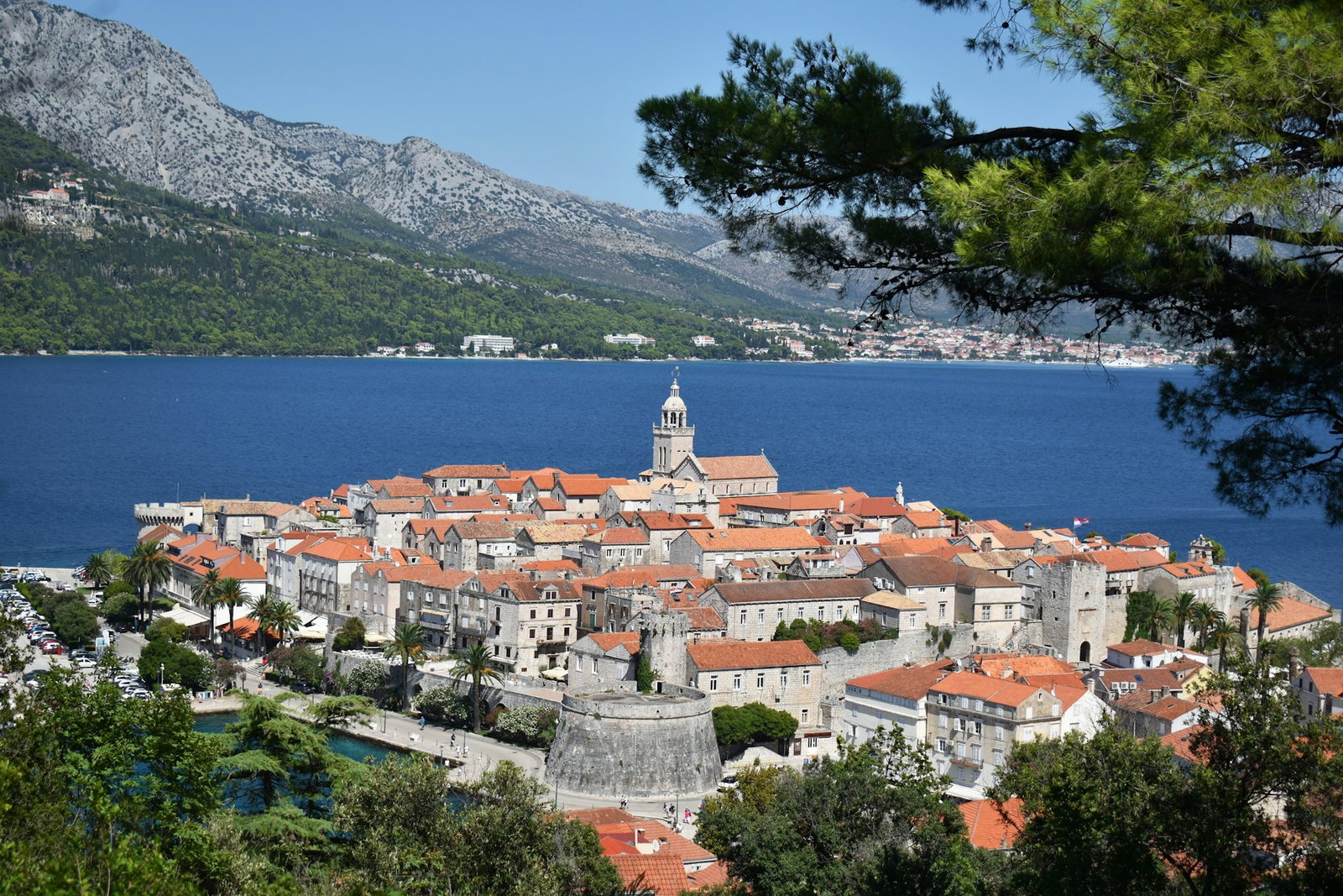 Scenic viewpoint of Korcula Old Town with island in distance, blue sea and dark green forest