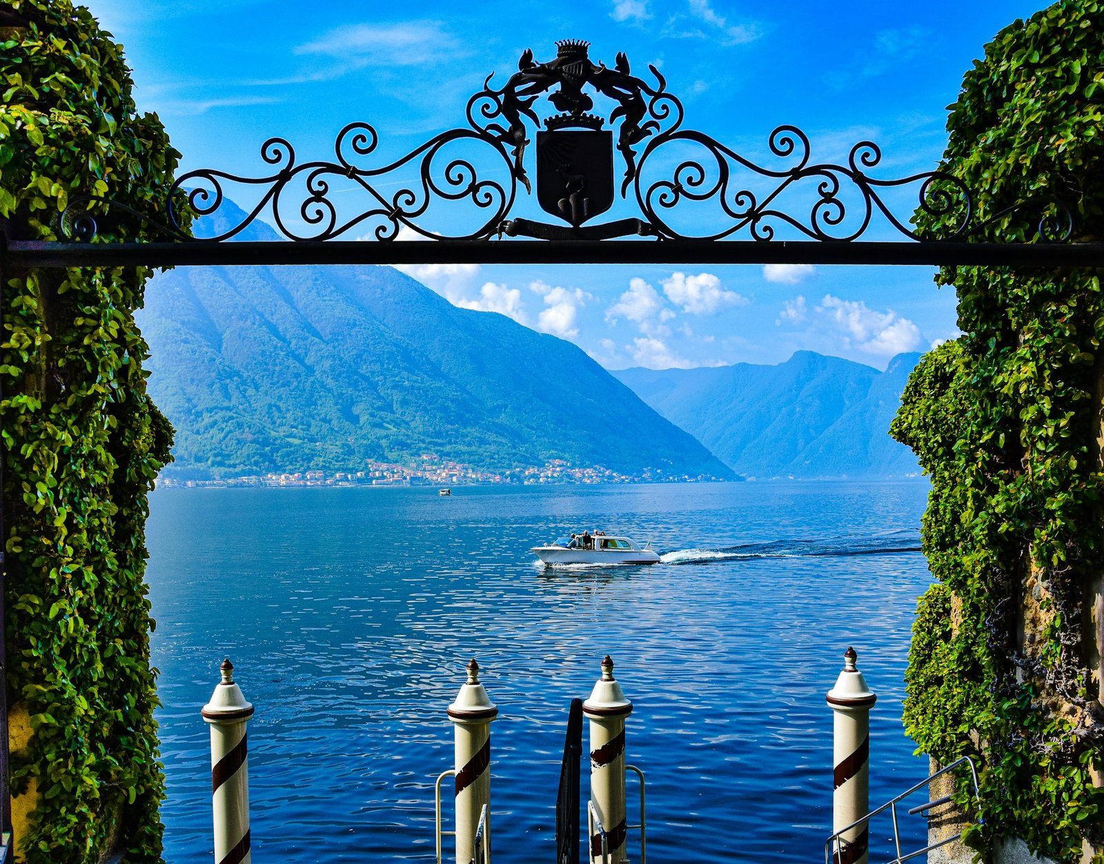 Garden leading out to deep blue waters with a boat gliding in the centre surrounded by valleys on a cloudy blue sky day