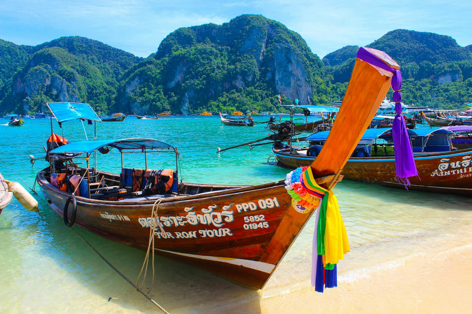Traditional longtail boat with rainbow decorations and docked in bright turquoise waters with more boats and limestone cliffs
