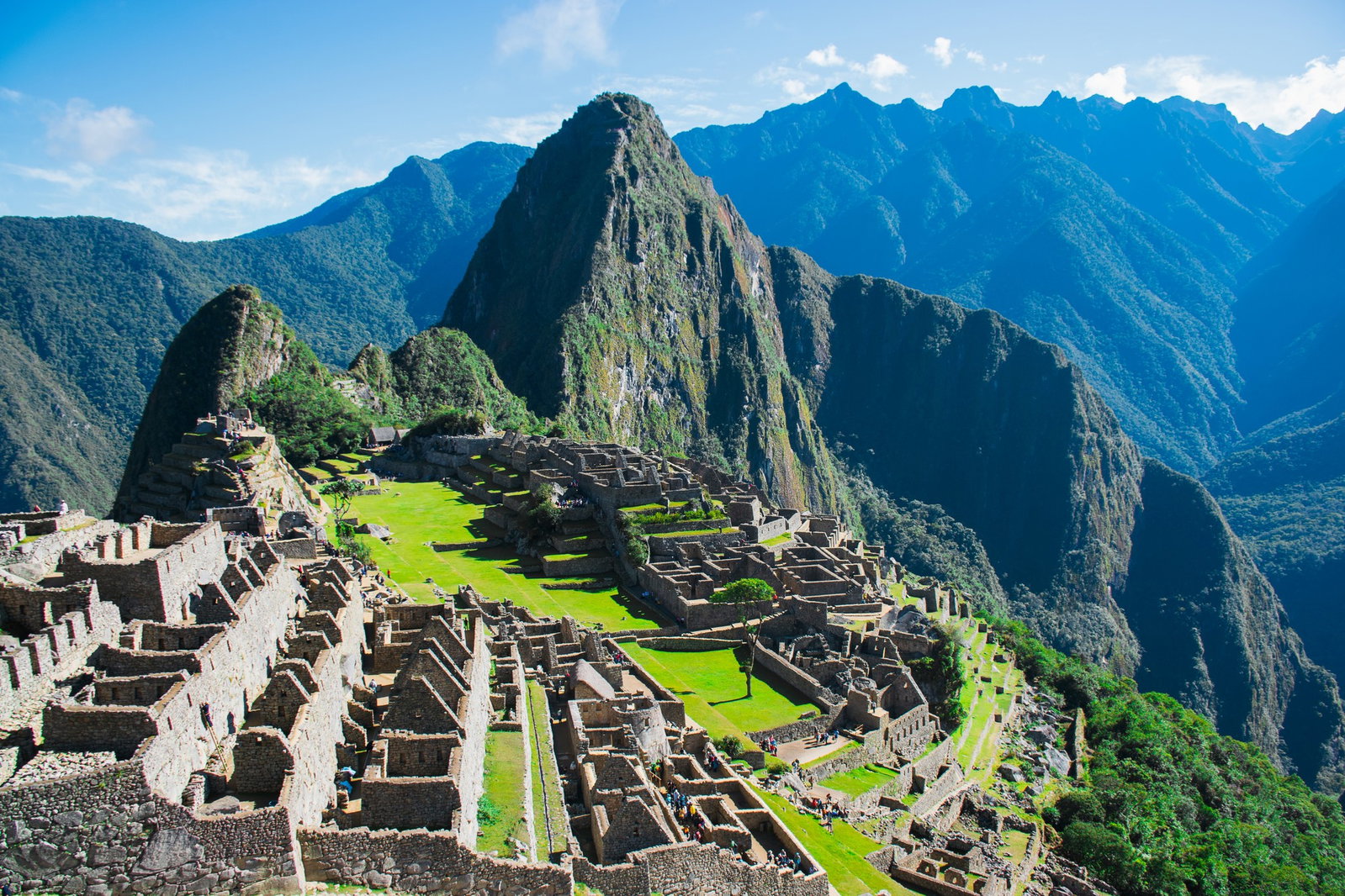 Maze of ancient stone ruins on emerald hills with towering green mountains and blue skies