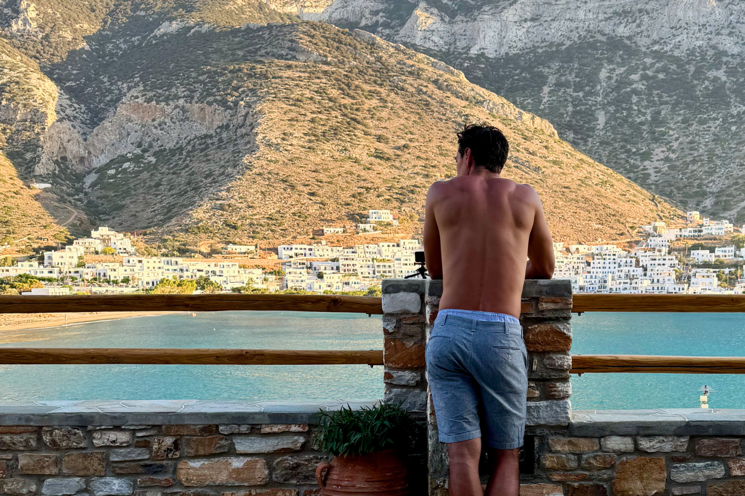 Traveller looking out to blue sea and white buildings against mountains in greece