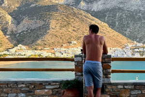 Traveller looking out to blue sea and white buildings against mountains in greece